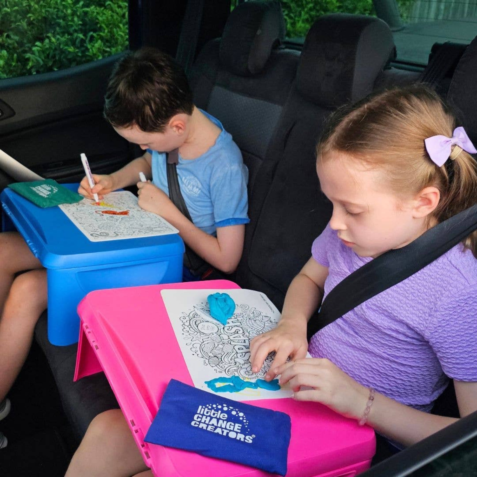 Two children sitting in a car, coloring with coloring books and crayons.