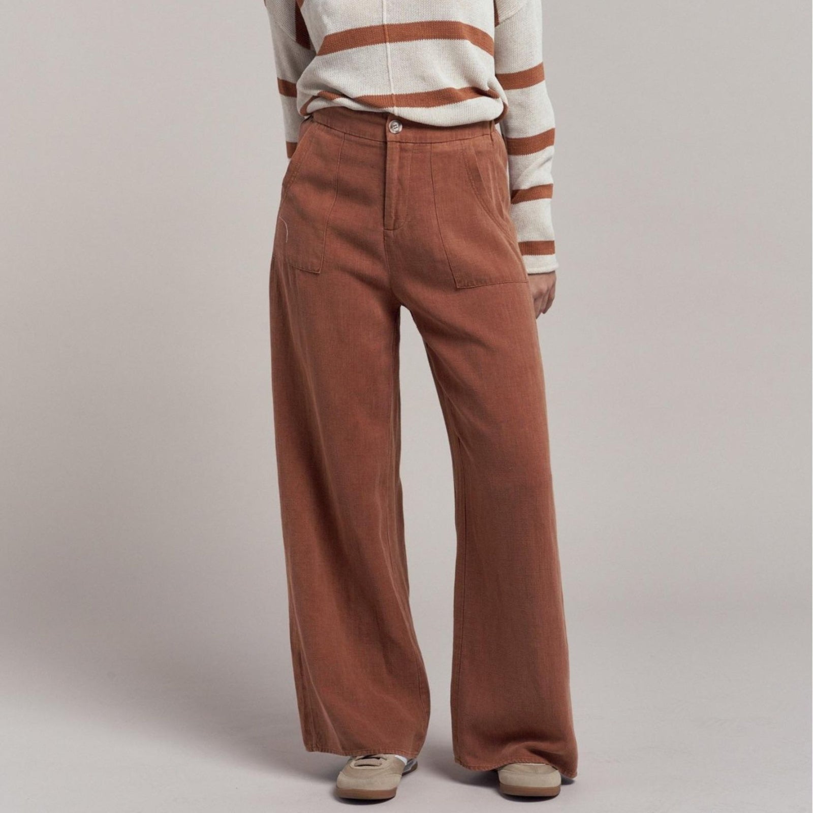 Woman wearing a beige shirt and pants against a plain background