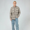 Man wearing a plaid shirt, light blue jeans, and brown shoes on a white background
