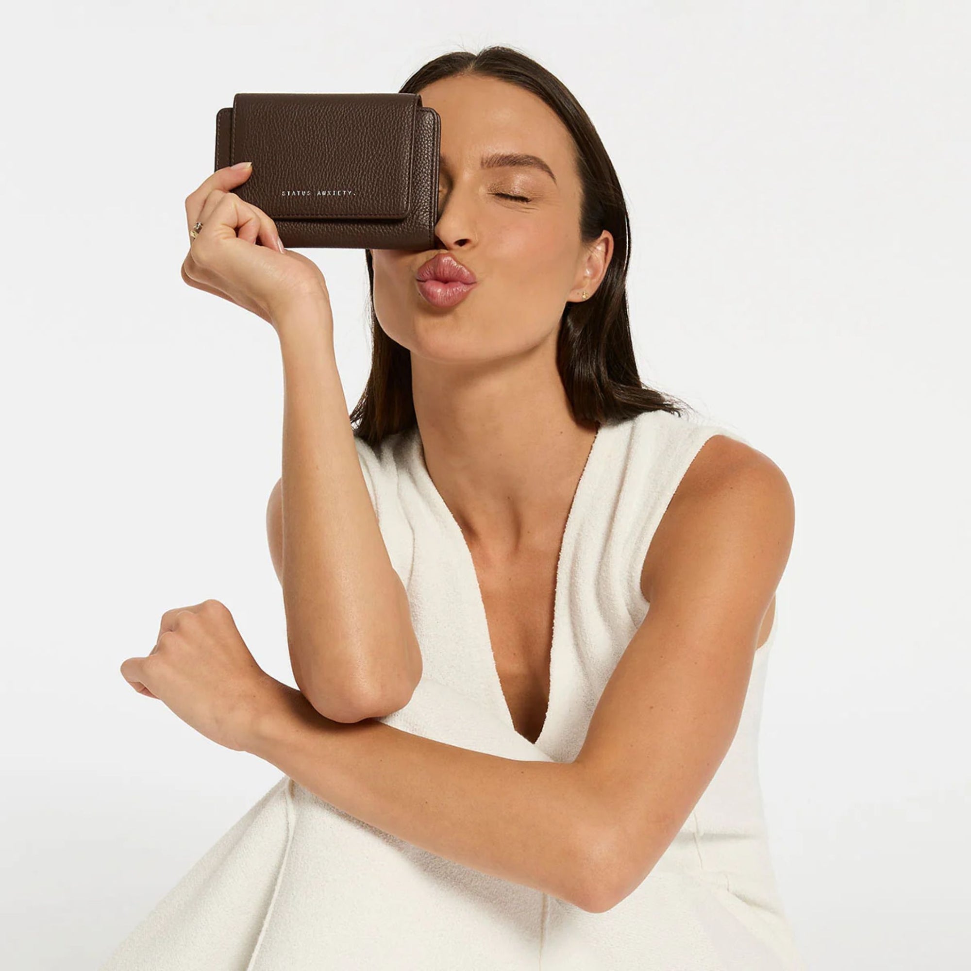 Woman holding a brown wallet up to her face on a white background