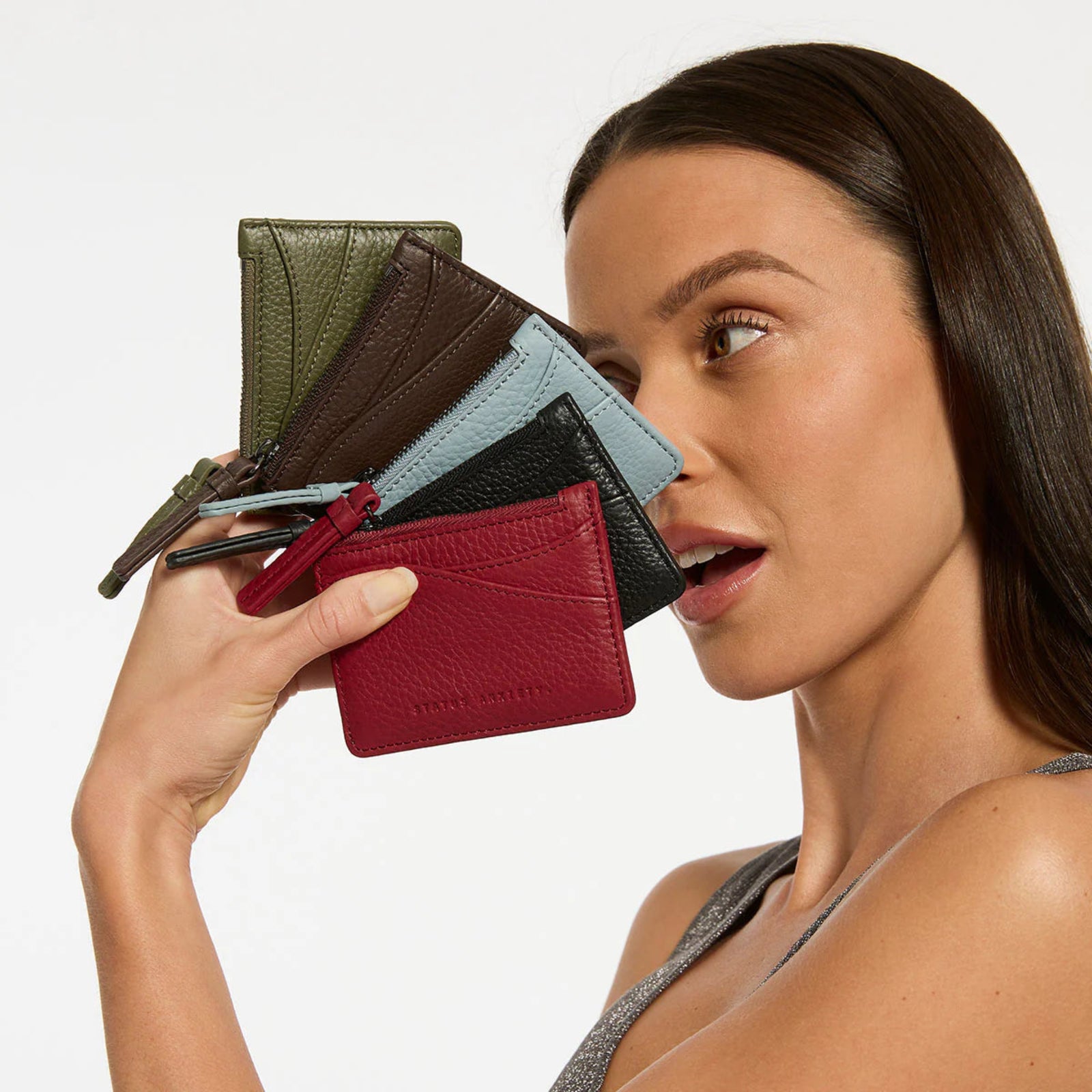 Woman holding multiple leather wallets of different colors against a neutral background