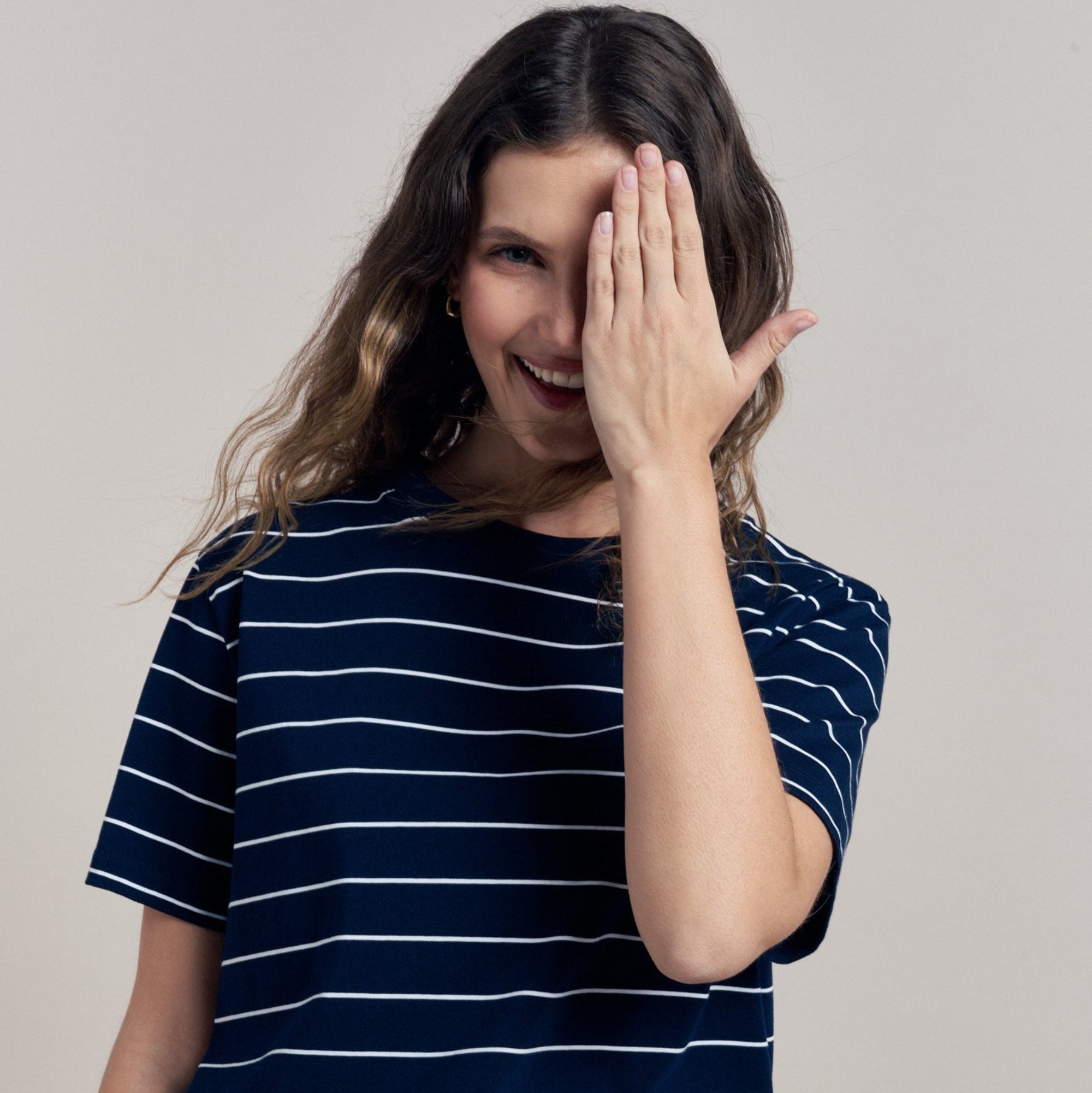Woman wearing a navy striped t-shirt and beige pants against a neutral background