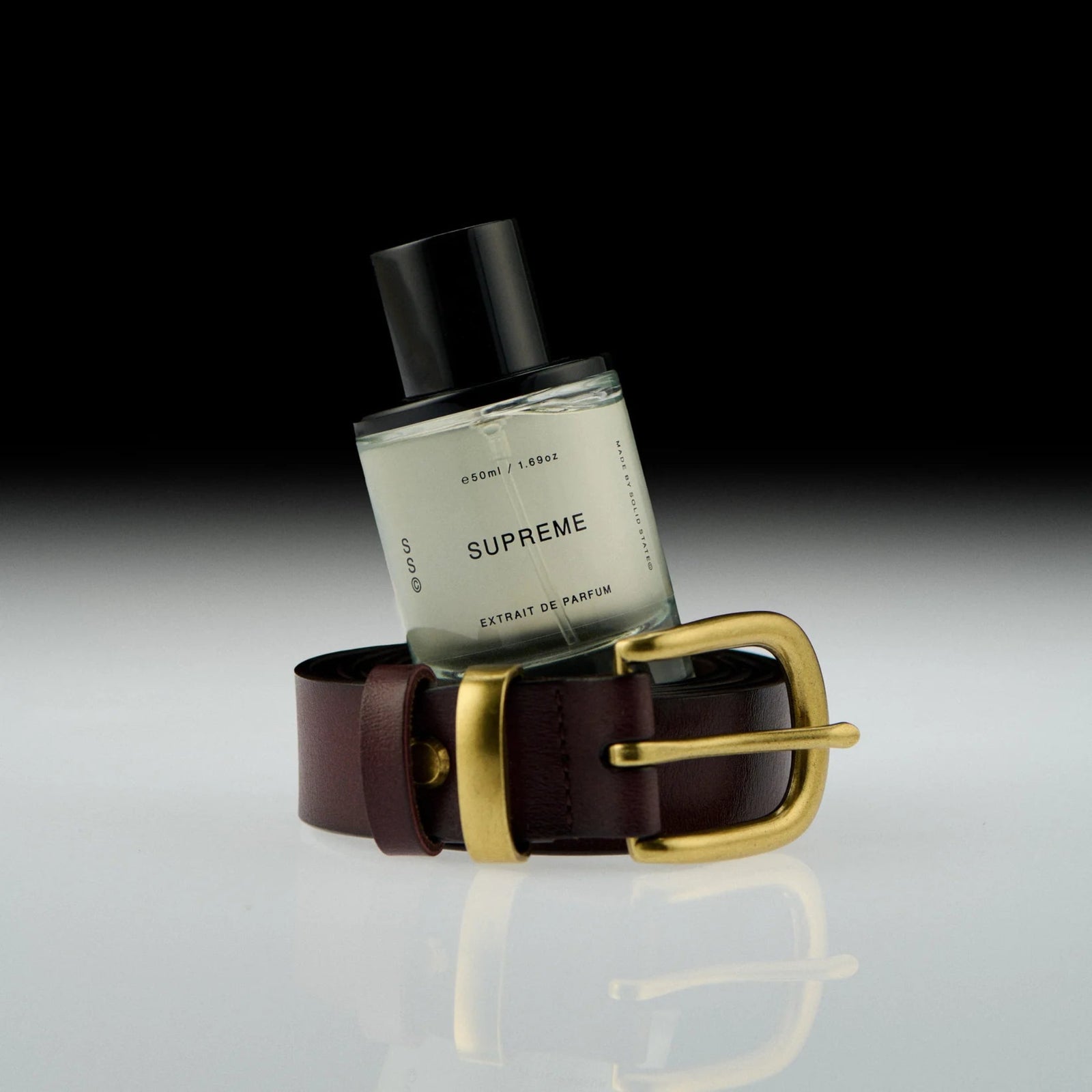 Perfume bottle labeled 'Supreme' with a brown leather belt and gold buckle on a gradient background